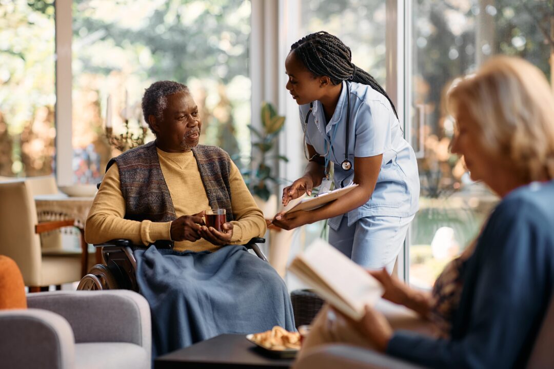 A nurse holding a clipboard, speaking to a care home resident.