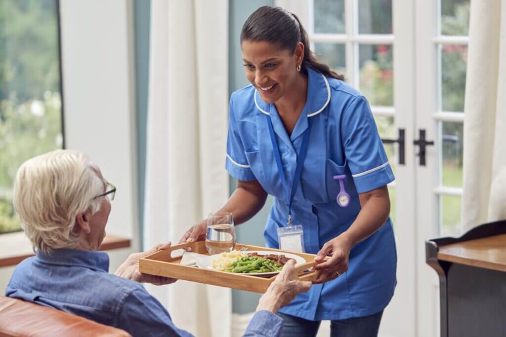 A nurse handing an elderly person a tray of food