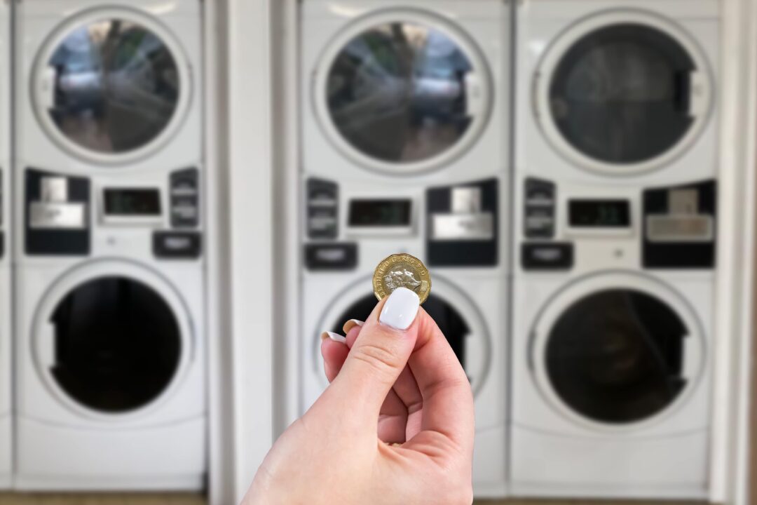 hand holding a one-pound coin in front of commercial laundry machines.